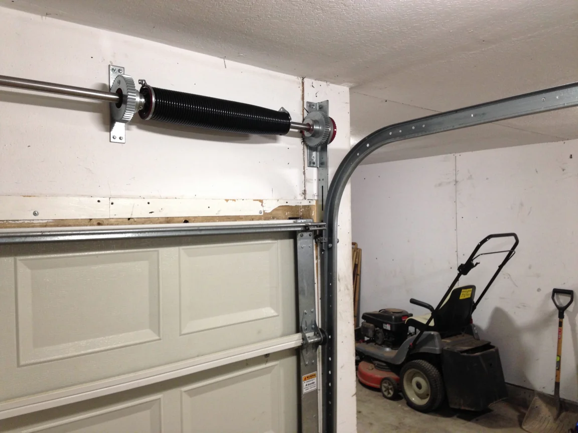 A black torsion spring is mounted above a white garage door.